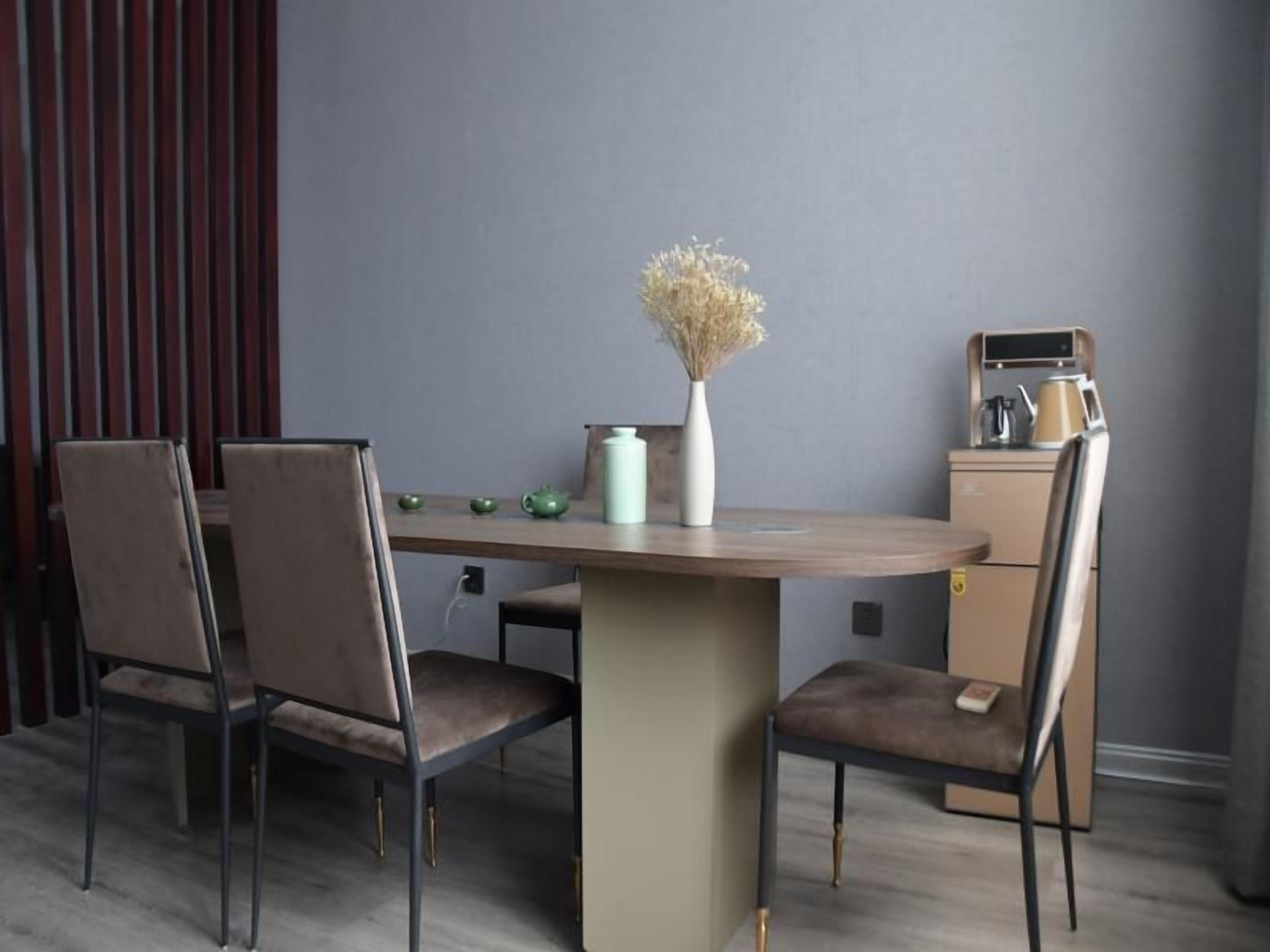 A dining area with a round table, four chairs, a vase with dried flowers, and a coffee machine.
