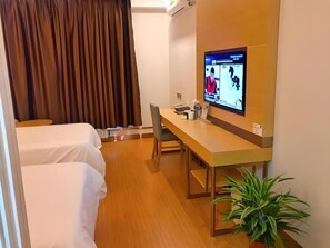 Une chambre d’hôtel avec deux lits, un bureau avec un ordinateur, une chaise, une plante en pot et un rideau.