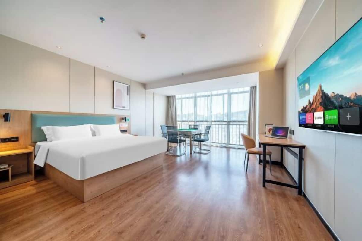 A modern hotel room with a large bed, a desk, and a balcony with a view.