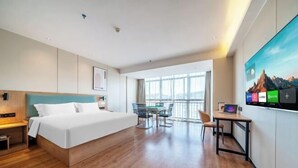 A modern hotel room with a large bed, a desk, and a balcony with a view.