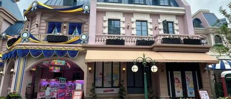 A building with a pink facade, a balcony with black railings, and a storefront with a sign.