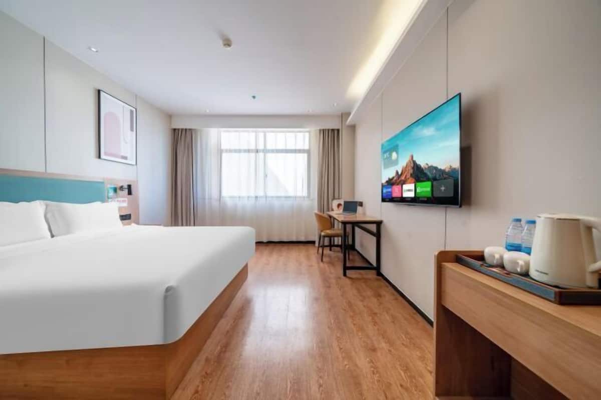 A hotel room with a bed, a desk, a chair, a television, and a window with curtains.