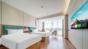 A modern hotel room with a large bed, two smaller beds, a TV, and a view of the outdoors.