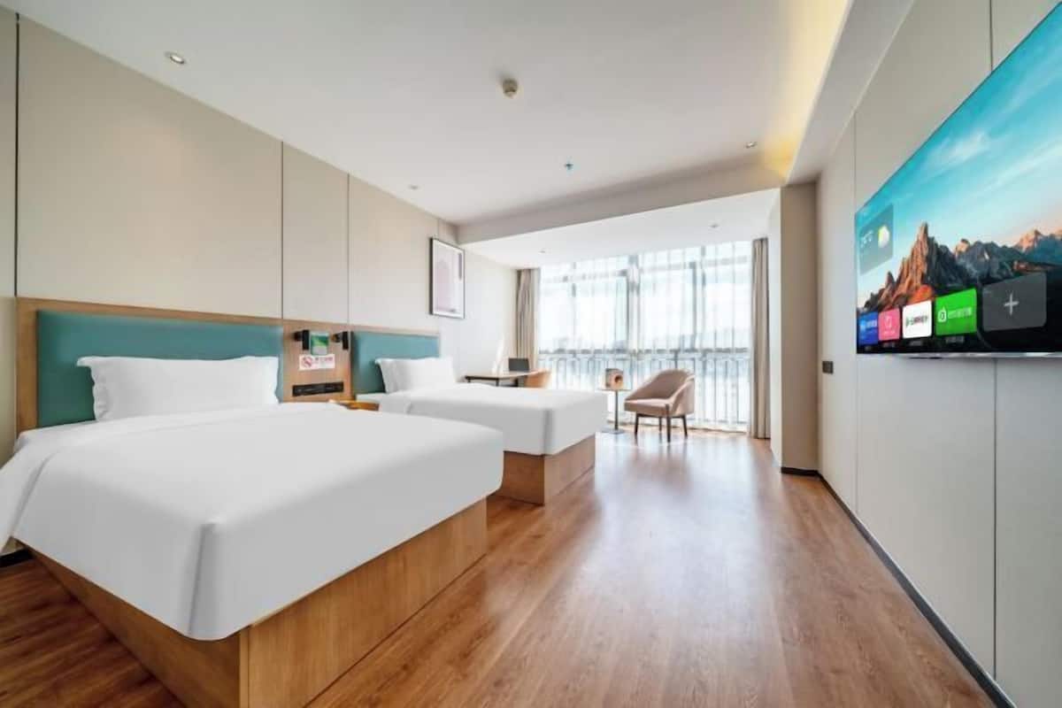 A modern hotel room with a large bed, two smaller beds, a TV, and a view of the outdoors.
