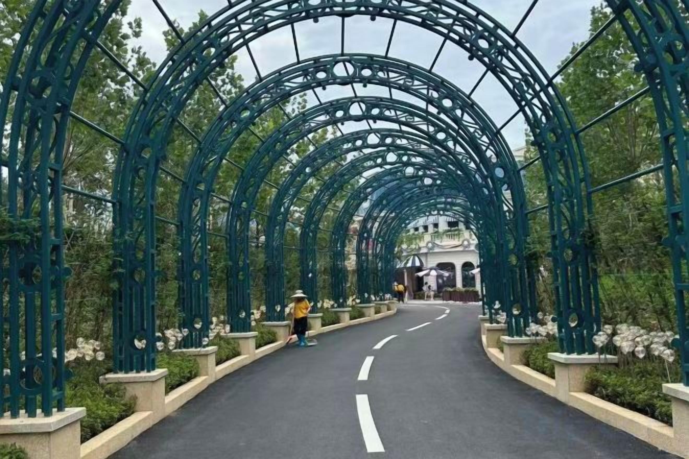 A pathway with a metal archway, lined with greenery and leading to a building.