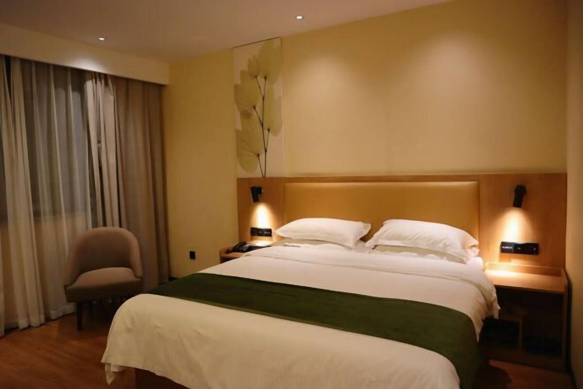 A hotel room with a large bed, two bedside tables with lamps, a chair, and a wall-mounted artwork.