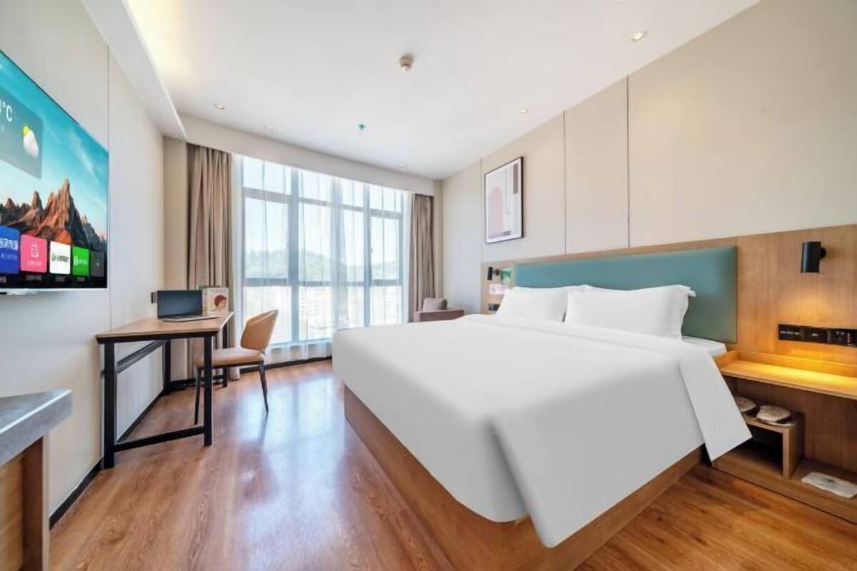 A hotel room with a bed, a desk, a chair, a TV, and a window.