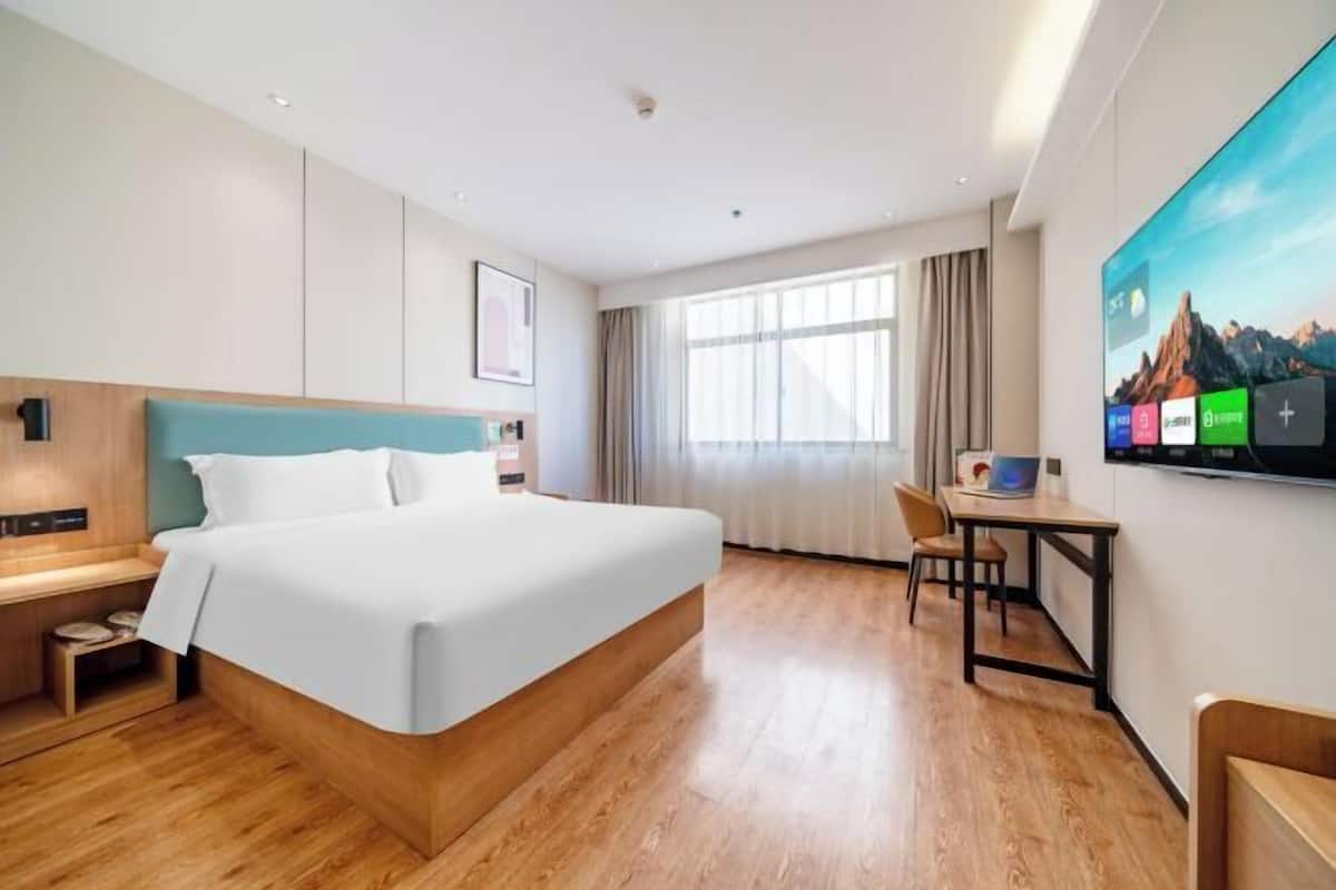 A hotel room with a bed, a desk, a chair, a TV, and a window with curtains.