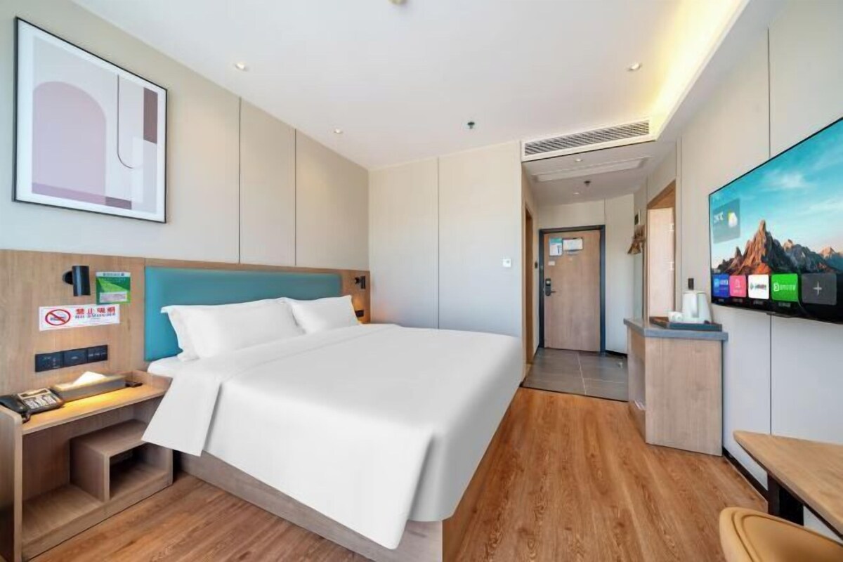 Una camera d'albergo con un letto, una scrivania, una televisione e un cartello appeso al muro.