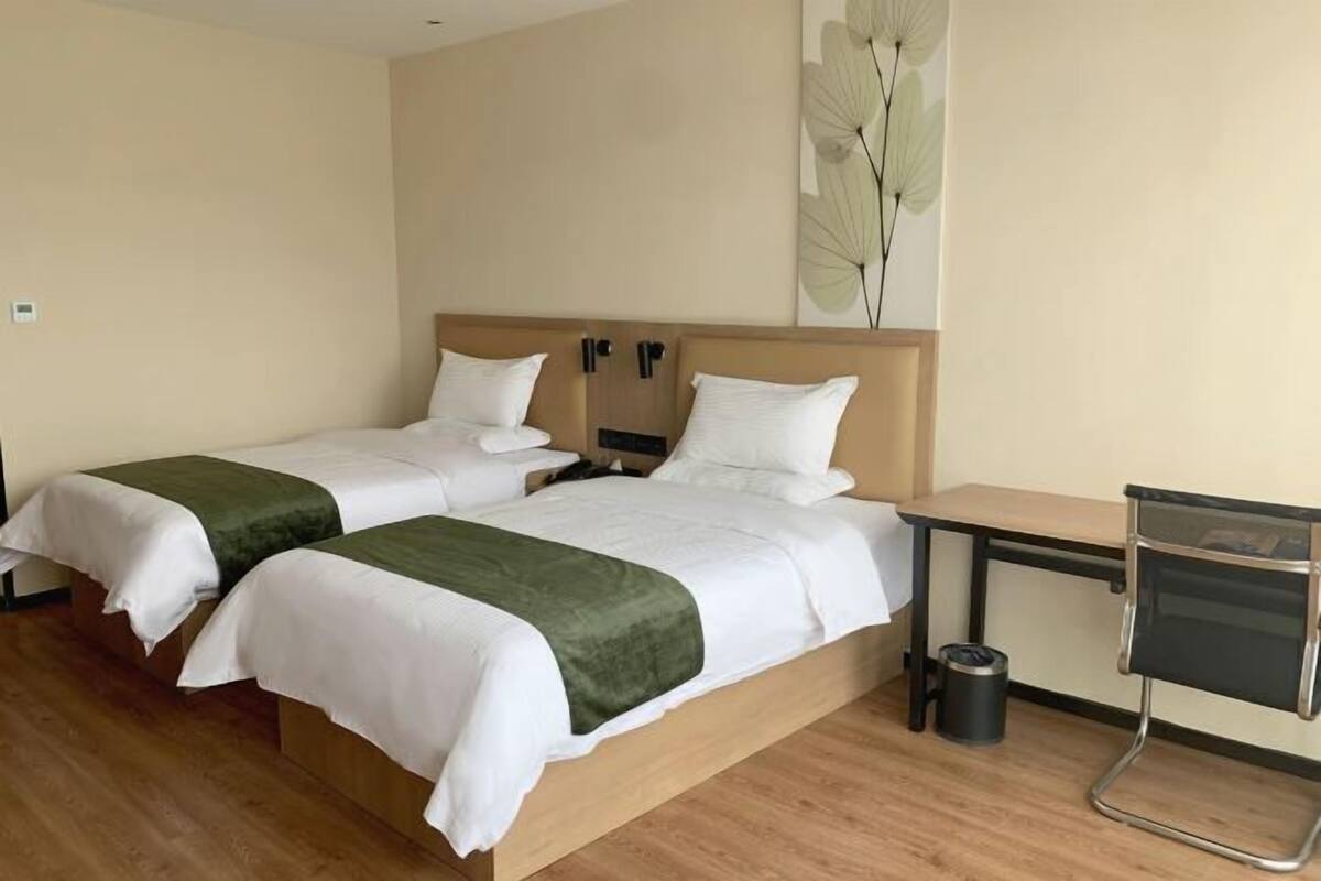 A hotel room with two single beds, a wooden desk, a chair, and a trash bin.