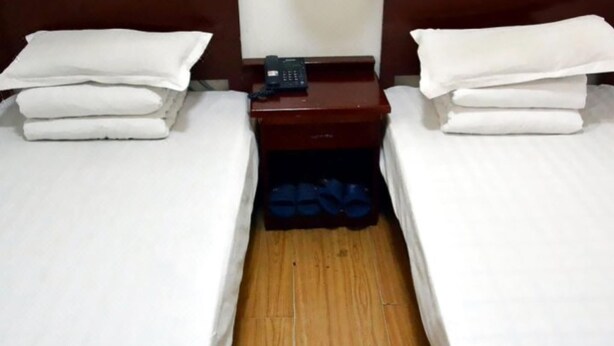 Quarto de hotel com duas camas de solteiro, mesa de cabeceira com telefone e um par de chinelos azuis.