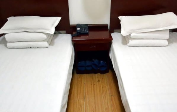 A hotel room with two single beds, a nightstand with a phone, and a pair of blue slippers.