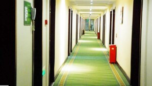 Corredor de hotel com portas em ambos os lados, carpete verde e uma lixeira vermelha.