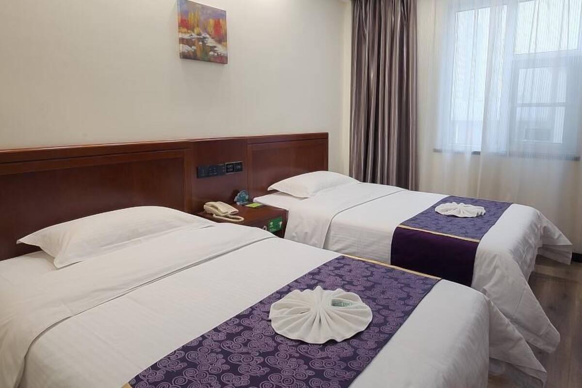 Ein Hotelzimmer mit zwei Betten, einem Bild an der Wand, einem Telefon auf dem Nachttisch und einem Fenster mit Vorhängen.