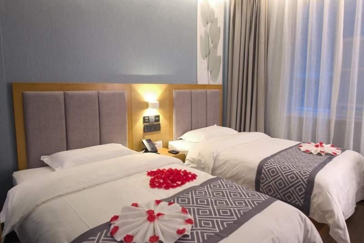 Ein Hotelzimmer mit zwei Betten, einem Kopfteil mit Beleuchtung, einem Nachttisch mit Telefon und einem Fenster mit Vorhängen.