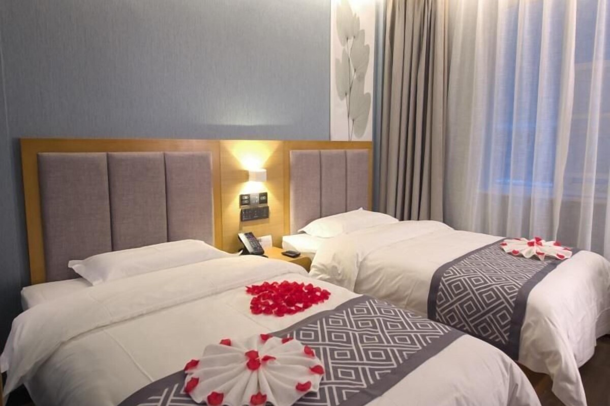 Ein Hotelzimmer mit zwei Betten, einem Kopfteil mit Beleuchtung, einem Nachttisch mit Telefon und einem Fenster mit Vorhängen.