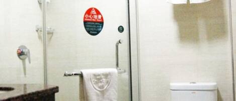 A bathroom with a glass shower enclosure, a toilet, and a sink with a towel hanging on the wall.