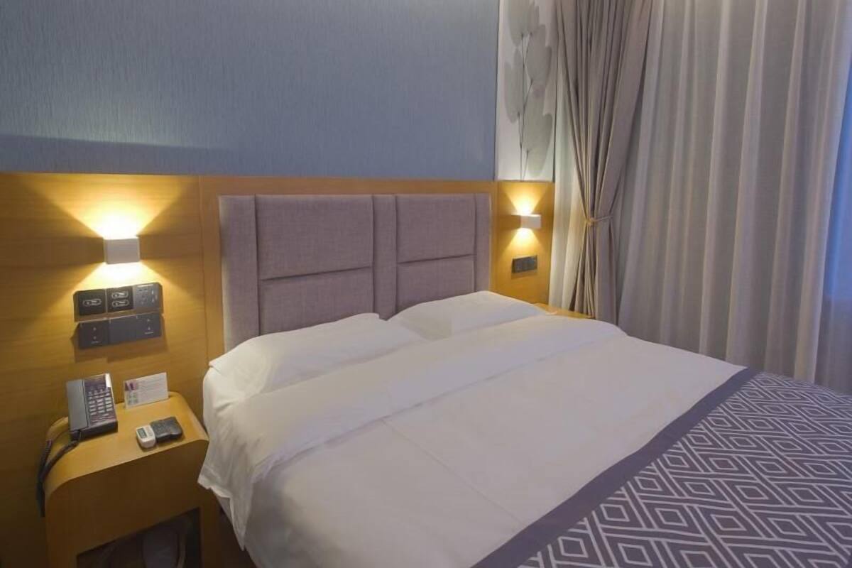 Ein Hotelzimmer mit einem Bett, einem Nachttisch mit Telefon und Lampe sowie einem Vorhang.