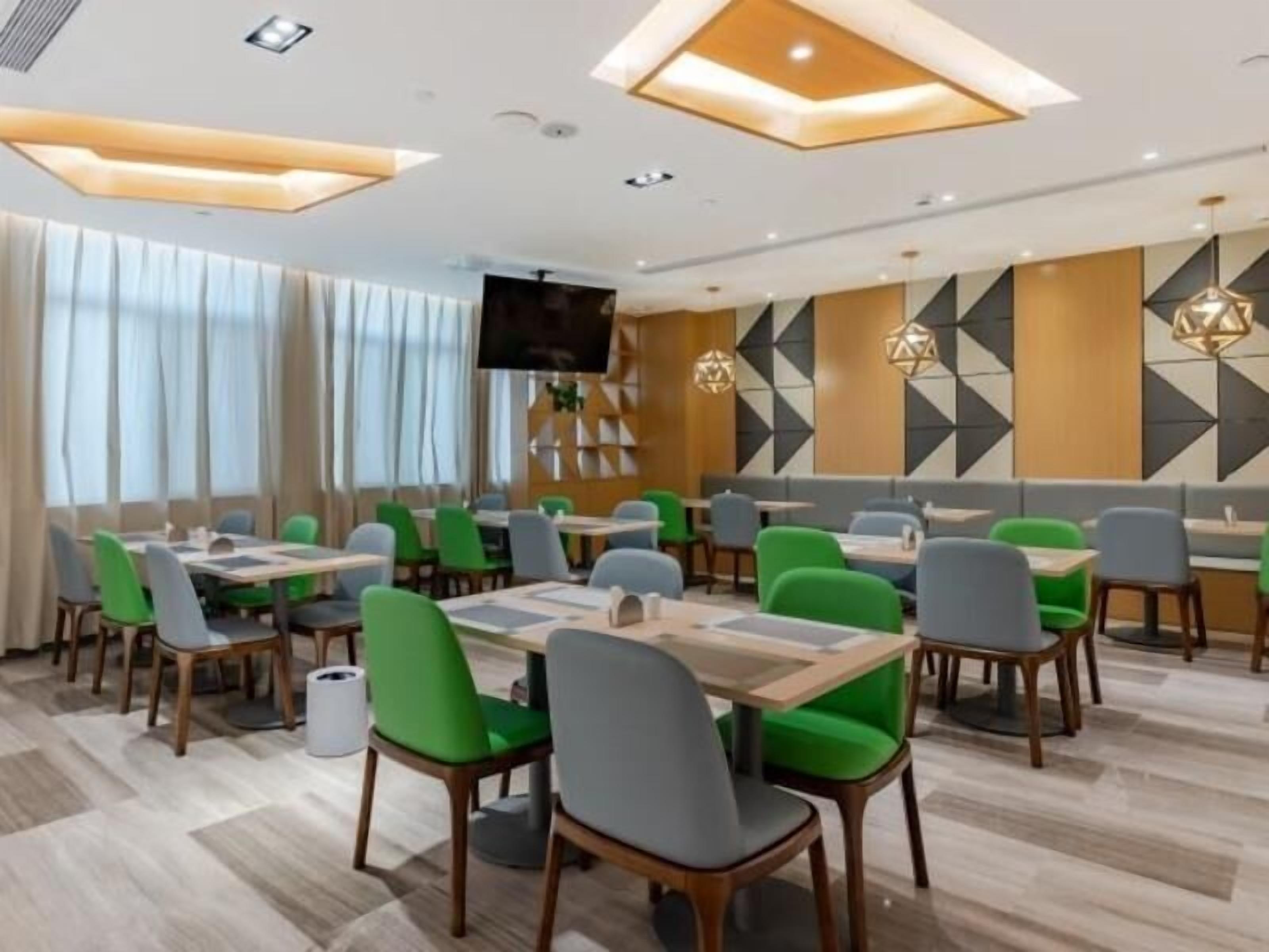 A modern restaurant with green and grey chairs, wooden tables, and geometric wall designs.