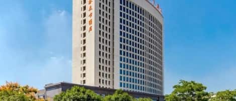 Un edificio alto y moderno con fachada de diseño geométrico y un rótulo en un alfabeto extranjero en el lateral.
