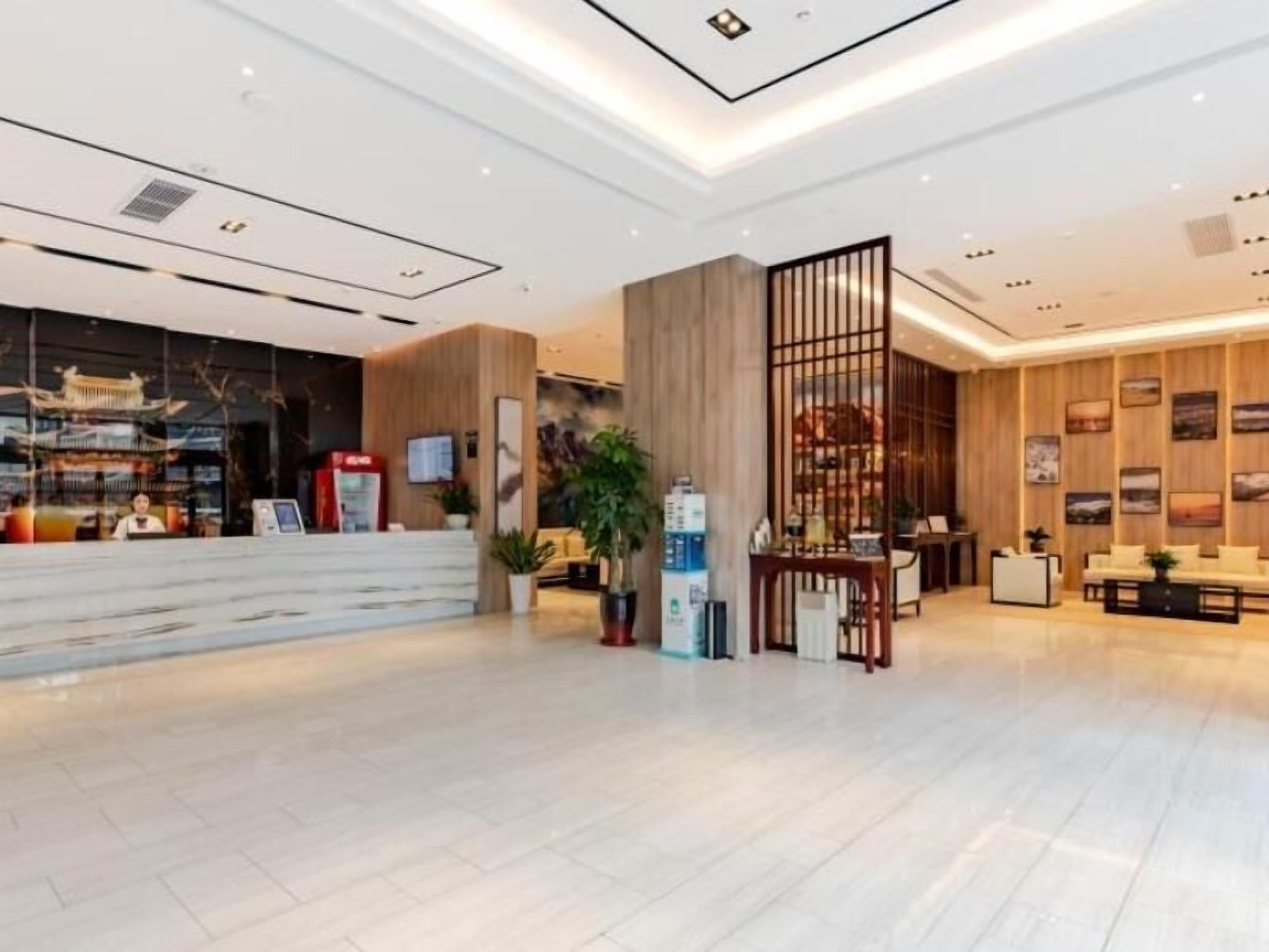 A modern hotel lobby with a reception desk, seating area, and a decorative wooden partition.