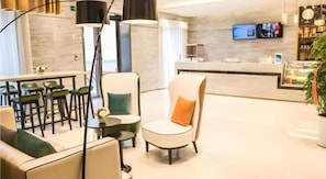A modern hotel lobby with seating arrangements, a reception desk, and a television screen.
