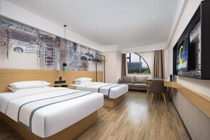 Habitación de hotel con dos camas, un sofá, un escritorio, un televisor y un mural en la pared.