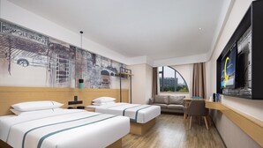 Et hotelværelse med to senge, en sofa, et skrivebord og et stort fjernsyn.