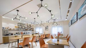 Et moderne spiseområde med flere borde og stole, et køkken i baggrunden og hængende lamper.