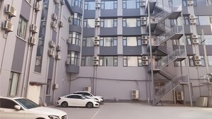 En bygning med flere etager, klimaanlæg, en hvid bil foran og en trappe på højre side.