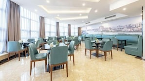 A spacious dining area with multiple tables and chairs, large windows with curtains, and a cityscape mural on the wall. - GreenTree Inn (Nantong Shanghe Plaza) (Nantong)