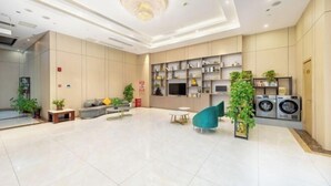 A spacious living area with a modern chandelier, a sofa, a teal armchair, a coffee table, and a TV mounted on the wall. - GreenTree Inn (Nantong Shanghe Plaza) (Nantong)