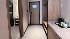 A narrow hallway with a wooden door, a small kitchenette with a countertop and a coffee machine, and a shelf with folded towels. - GreenTree Inn (Nantong Shanghe Plaza) (Nantong)