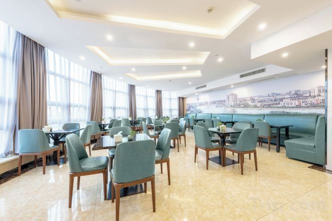 A spacious dining area with multiple tables and chairs, large windows with curtains, and a cityscape view.