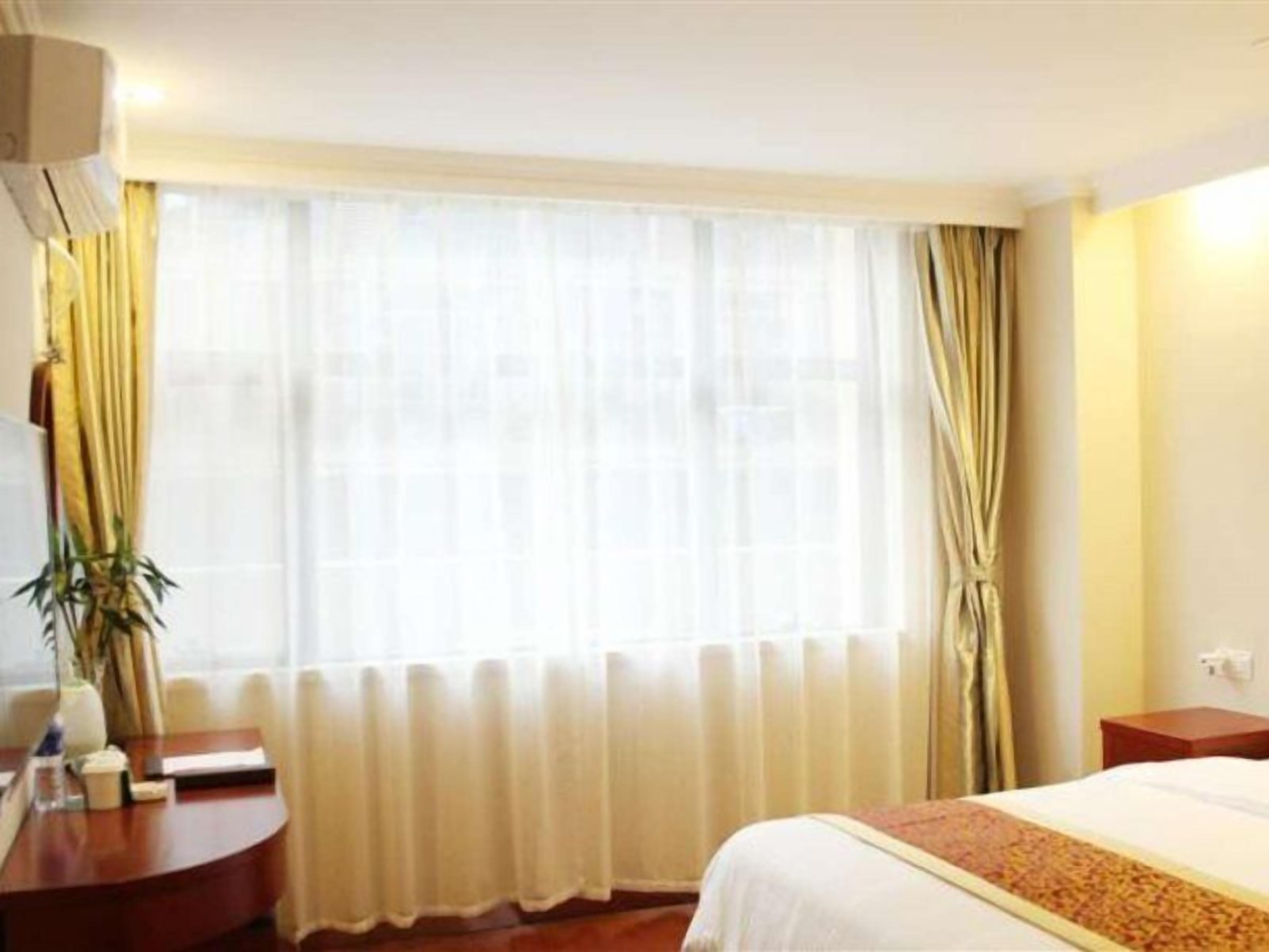 Habitación de hotel con cama, escritorio y ventana con cortinas.