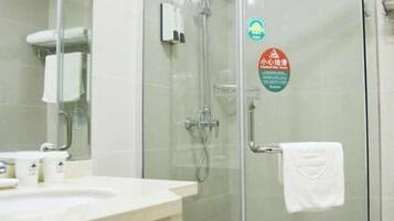 A bathroom with a glass shower enclosure, a white sink, and a towel hanging on the wall.