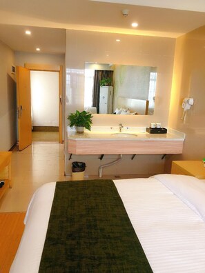 Een hotelkamer met een bed, een badkamer met een wastafel en spiegel, een potplant en een deur naar een andere kamer.