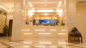 A reception area with a modern design, featuring a reception desk, multiple screens, and a decorative plant. - Greentree Inn Xinyang Gushi County Liaocheng Avenue (Xinyang)