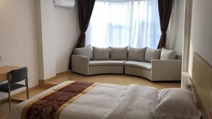 A hotel room with a bed, a curved sofa, a desk, and a window with curtains. - Greentree Alliance Texas Railway Station Municipal Hospital Hotel (Dezhou)