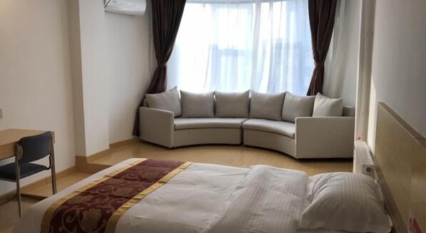 A hotel room with a bed, a curved sofa, a desk, and a window with curtains. - Greentree Alliance Texas Railway Station Municipal Hospital Hotel (Dezhou)
