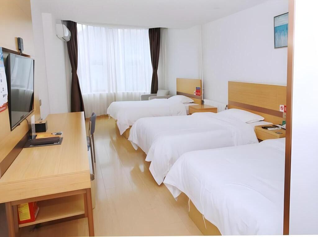 A hotel room with three single beds, a desk with a computer, a TV, and a window with curtains.