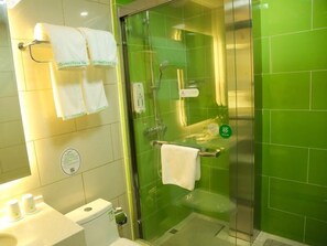 Een badkamer met groene tegels, een glazen douchecabine, een toilet en twee witte handdoeken aan haken.