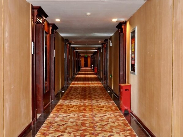 Un couloir d’hôtel avec un sol recouvert de moquette, des portes des deux côtés et une poubelle sur la droite.