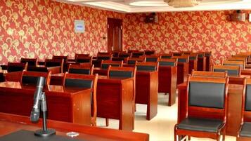 Un salón de conferencias con filas de sillas y mesas de madera, un atril y un papel tapiz estampado.