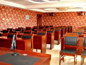 Un salón de conferencias con filas de sillas y mesas de madera, un atril y un papel tapiz estampado.