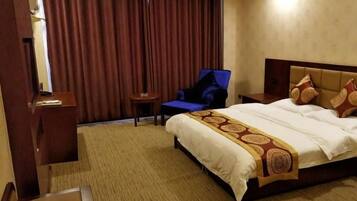 Habitación de hotel con una cama grande, una silla, una mesita y una cortina.