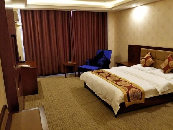 Habitación de hotel con una cama grande, una silla, una mesita y una cortina.