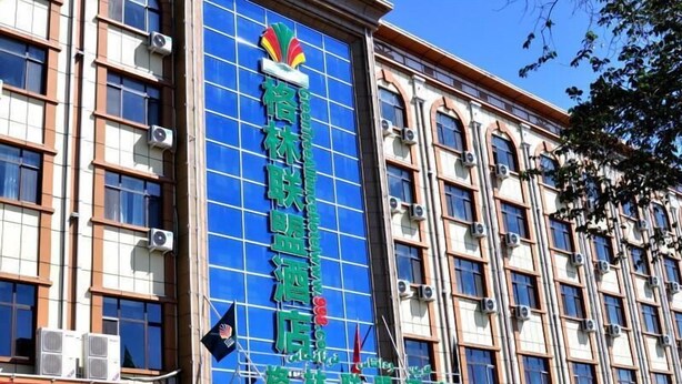 A hotel with a prominent blue glass facade, multiple air conditioning units, and a visible flag. - Greentree Alliance Hotel (Tacheng)