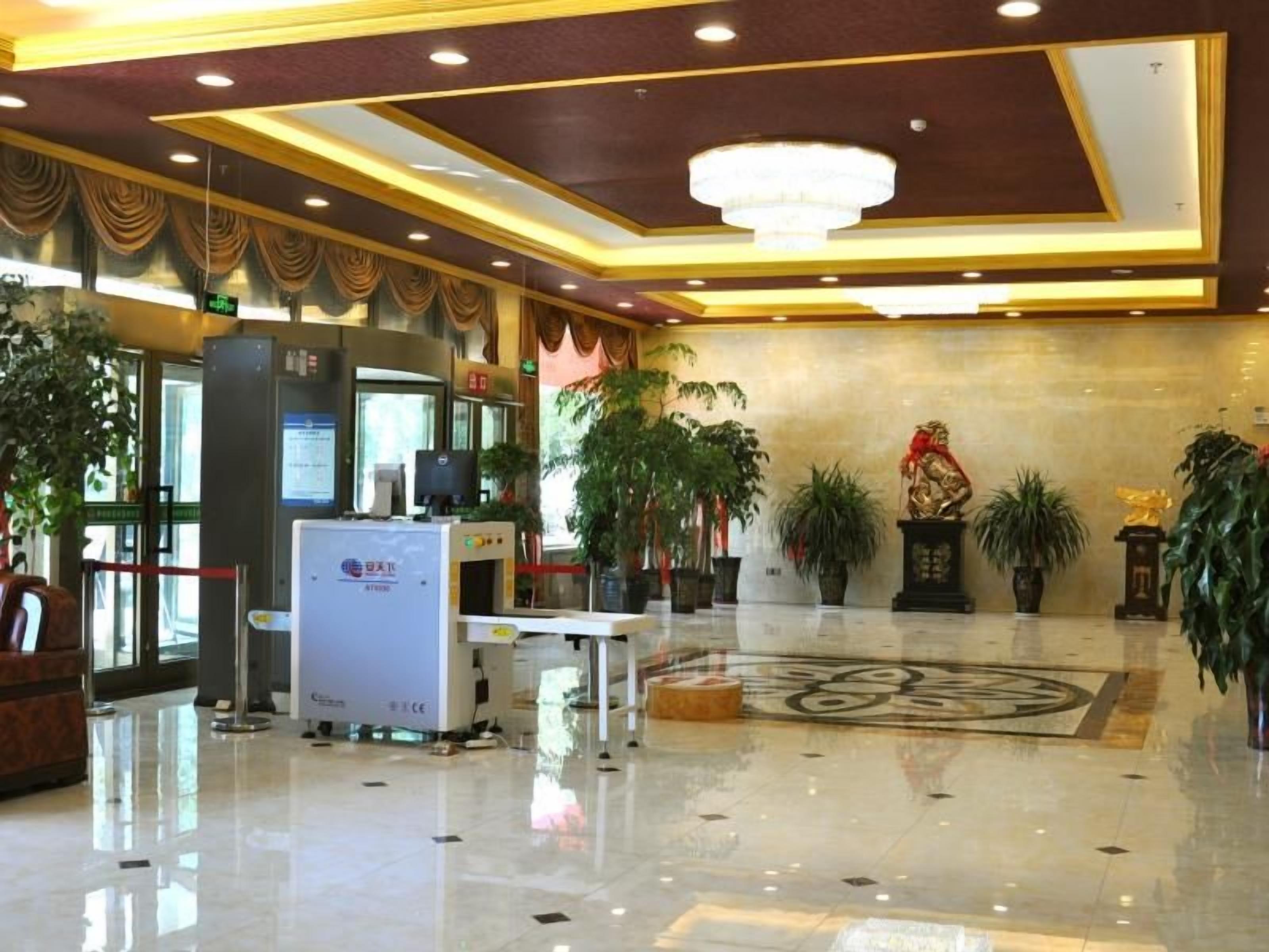 A hotel lobby with a reception desk, a large chandelier, and potted plants.