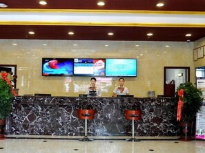 Zona de recepción de un hotel con un mostrador de mármol, dos recepcionistas y una pantalla grande mostrando contenido.
